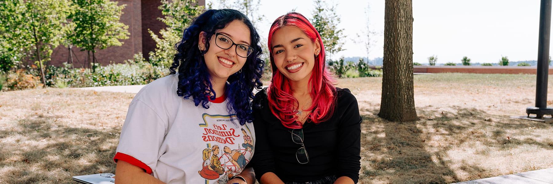 Two students smile sitting on the plaza